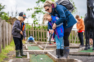 An image of a mum and her two children attempting to putt a hole at Cantref Adventure Farm's crazy golf course.
