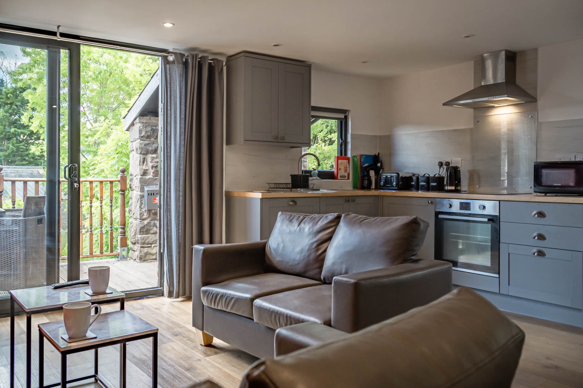 An image of a bright living area and kitchen inside a converted Hayloft, with French doors to a veranda with stunning views and outdoor seating.