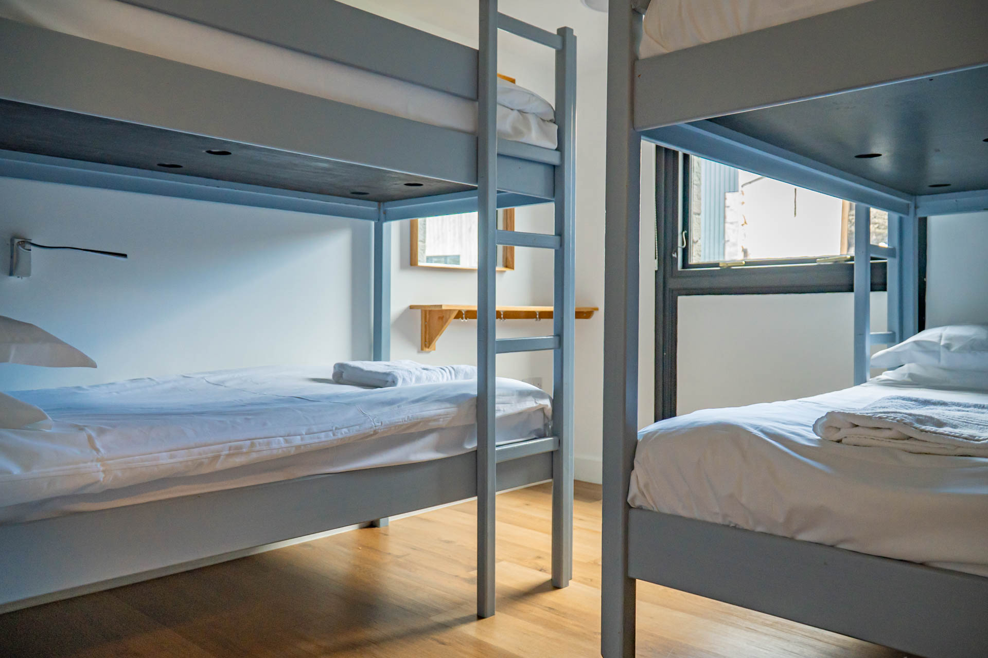 An image of two grey bunk beds with white linen and natural light from a rear window.