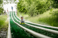 An action shot of a boy zooming down a wet artificial grass slide in a sledge, whilst being sprayed in the face with sprinklers.