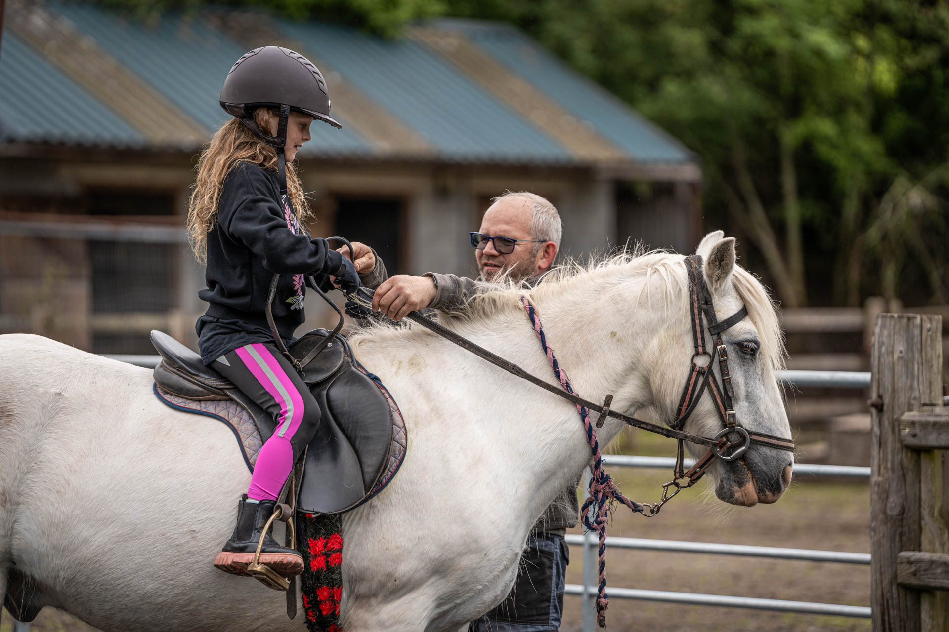 An image of a girl seated on a small white horse, having the reins checked by a member of the Cantref team.