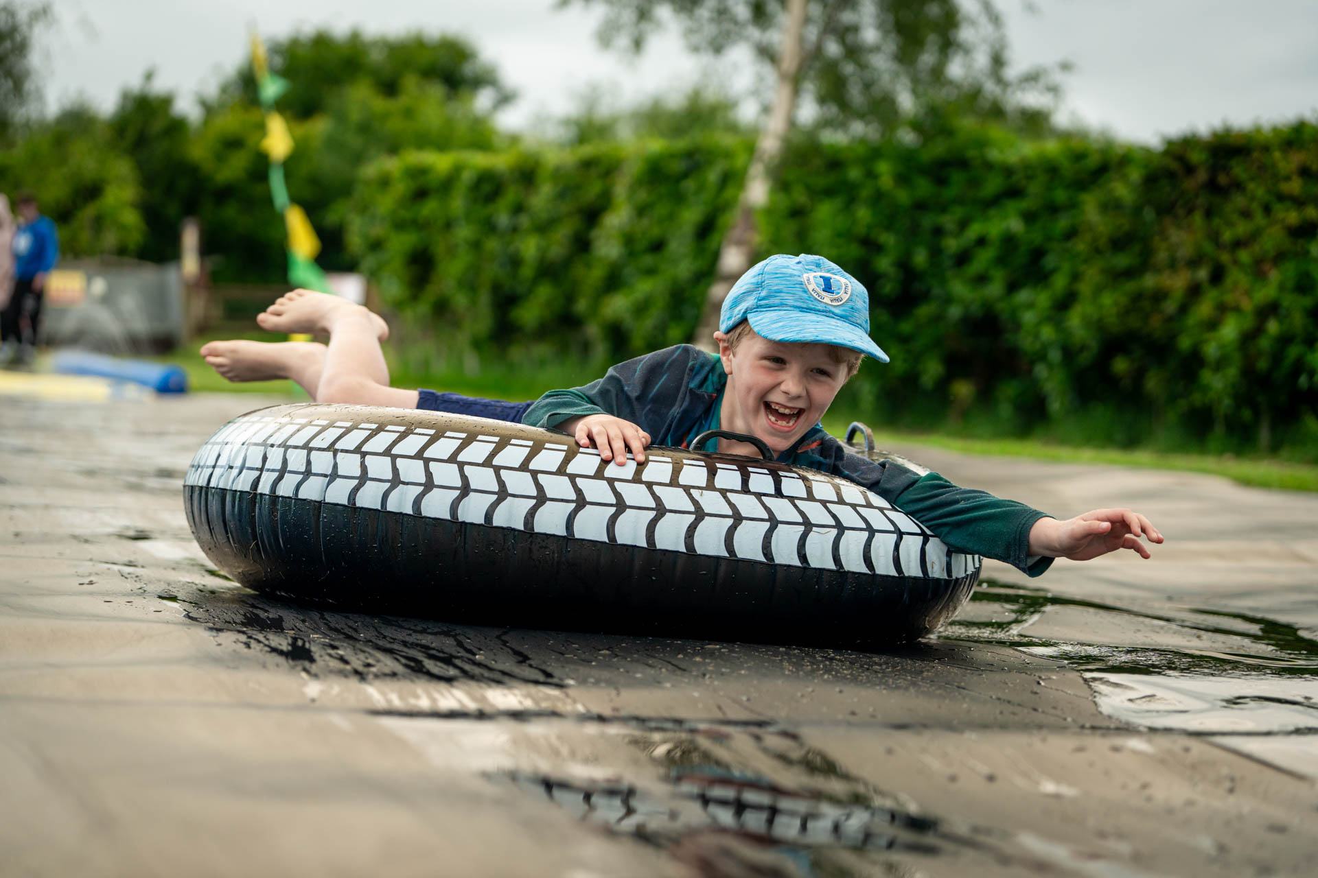 An image of a boy on an inflatable doughnut, sliding down a soapy slide, with a massive smile on his face.
