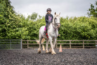 An image of a girl riding a small white horse around Cantref Riding Centre's training area.