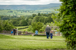 An image of grandma and toddler walking down to the sand and water play area, with rolling green hills for scenery.