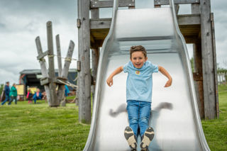 An image of a boy zooming down a giant silver reflective slide with a big smile on his face.