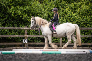 An image of a girl riding a small white horse around Cantref Riding Centre's training area.