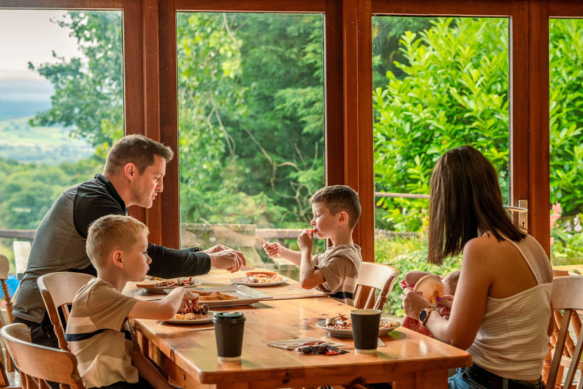 An image of a family of five having breakfast together, with a beautiful view out the full length windows.