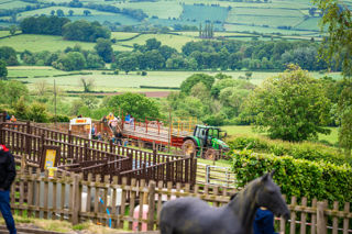 An image of a green tractor with a red trailer dropping off passengers from the tractor & trailer ride at Cantref Adventure Farm. There's a stunning backdrop of the Brecon countryside behind.