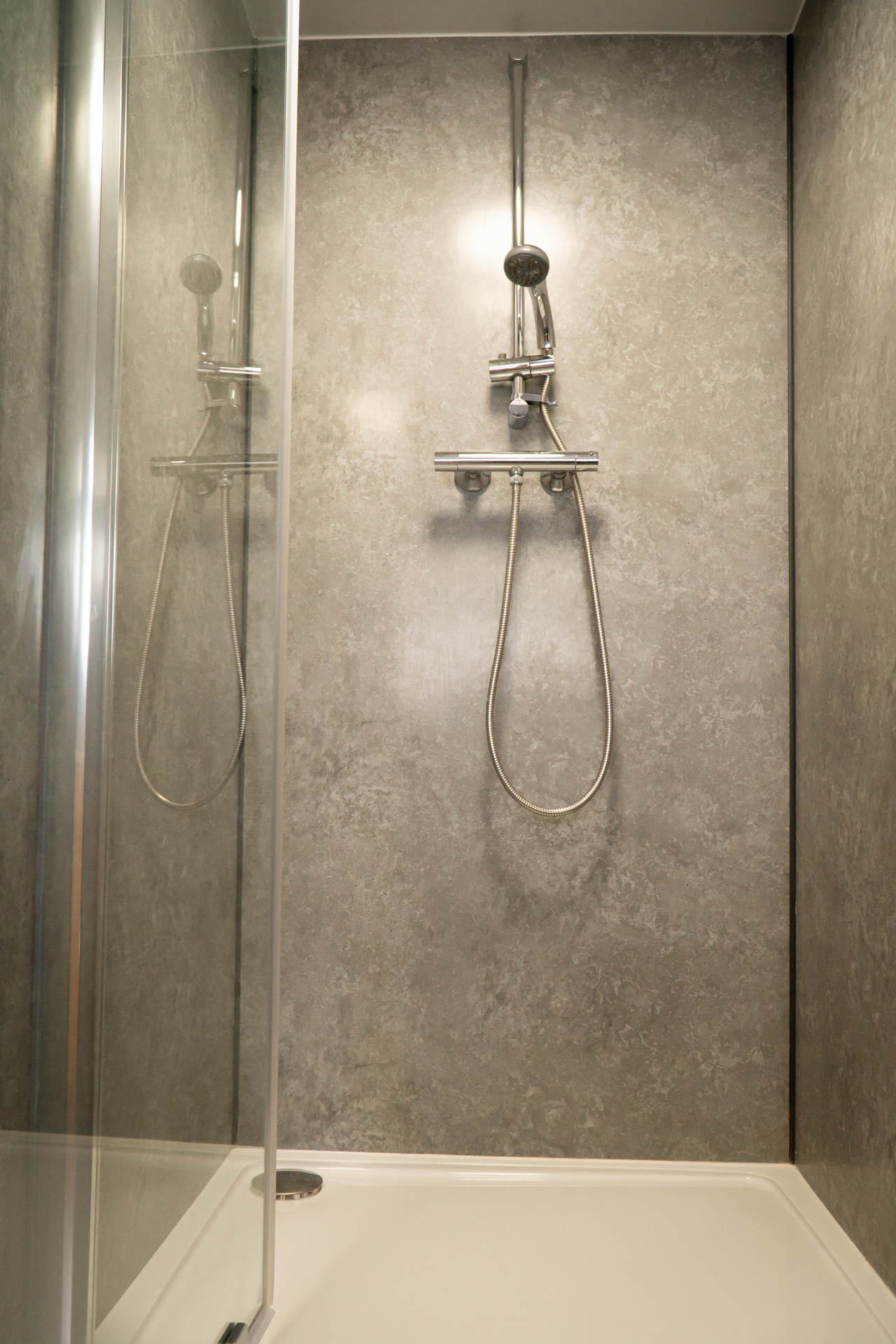 An image of a shower with stone effect walls, chrome fixtures and a white tray.