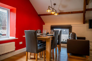 An image of The Milking Parlour's dining and living area, with red feature wall, leather chairs and sofas, Eddison bulb lighting and lots of natural light.