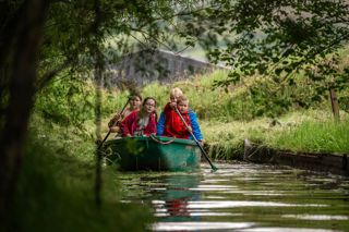 An image of four children and an adult in a green row boat, going round a jungle swamp course at Cantref Adventure Farm.