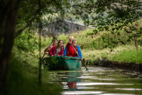An image of four children and an adult in a green row boat, going round a jungle swamp course at Cantref Adventure Farm.
