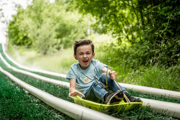 An action shot of a boy zooming down a wet artificial grass slide in a sledge.