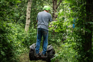 An image of a man on a Segway going down a path through the woods.