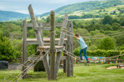 An image of a boy balancing on a rope bridge, with a wonderful panoramic view of the Brecon Beacons behind.