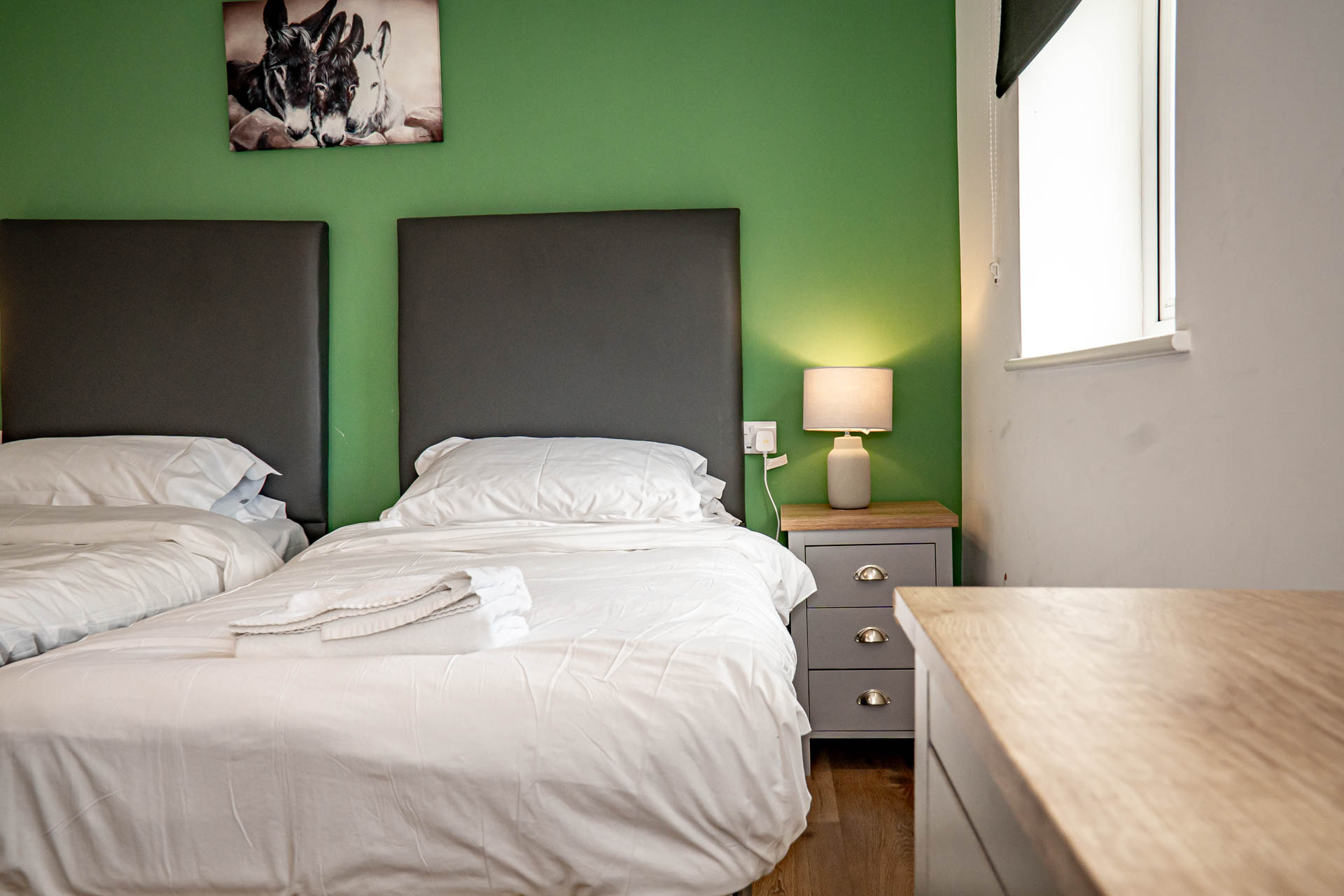 An image of a twin bedroom, with white linen and towels and a feature green wall.