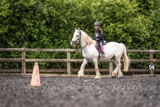 An image of a girl riding a small white horse around Cantref Riding Centre's training area.