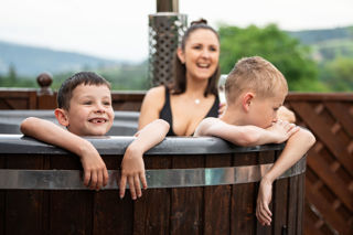 An image of mum in a woodfired hot tub with her two sons, with their arms over the side, with big smiles.