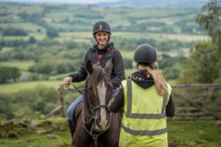 An image of the ride guide taking a requested photo of a woman on horseback against the beautiful Brecon backdrop.