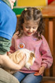 An image of a girl excitedly having a guinea pig placed on her lap.