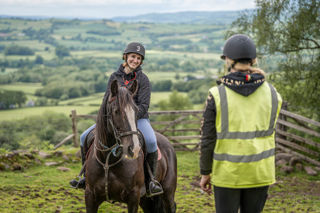 An image of a woman on horseback talking to the ride guide, with a beautiful view behind them.