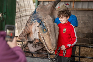 An image of a boy with a big smile on his face as he gets to hold blue the velociraptor and have their photo taken together, at Cantref Adventure Farm.