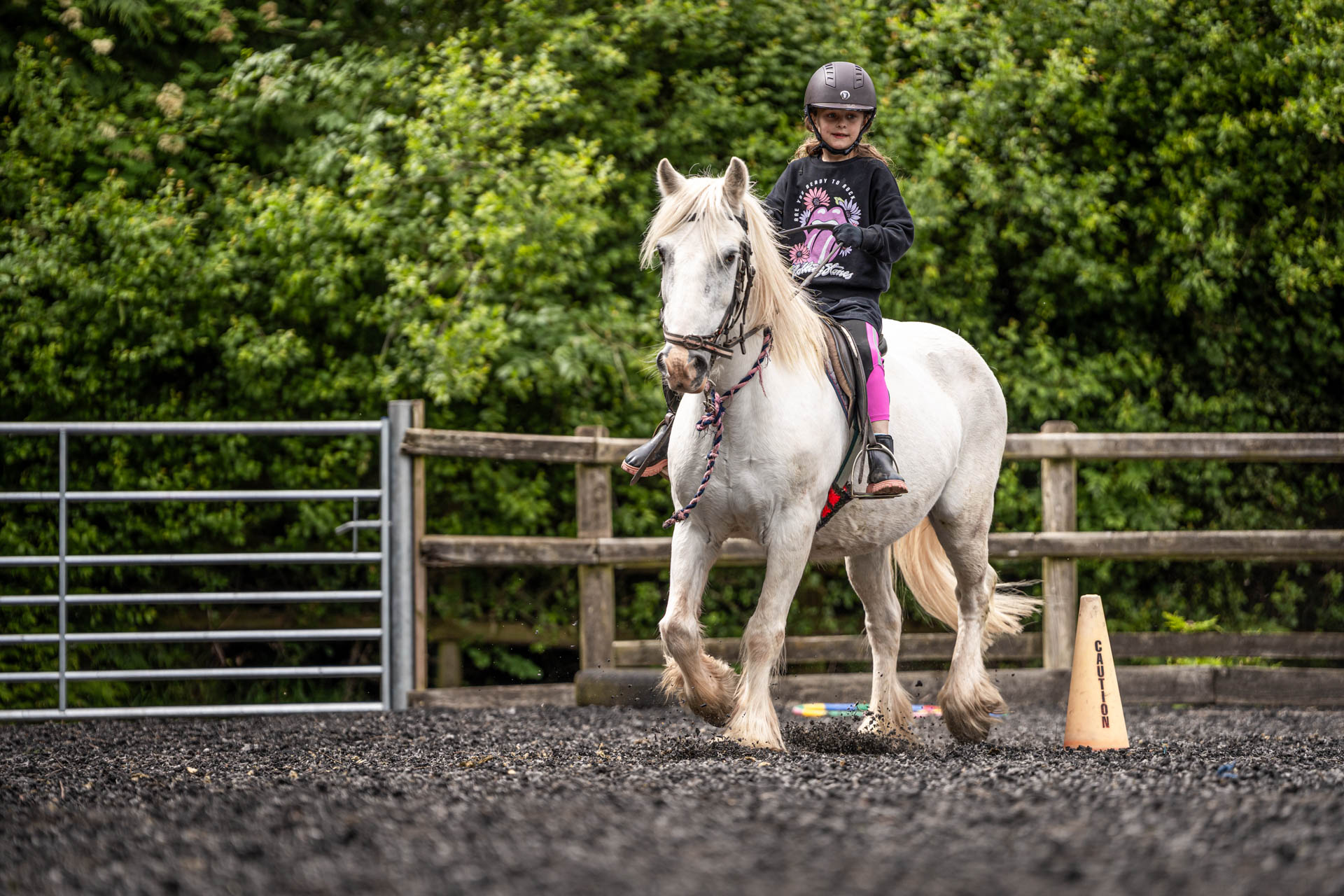 An image of a girl riding a small white horse around Cantref Riding Centre's training area.