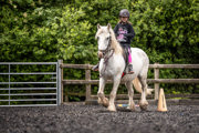 An image of a girl riding a small white horse around Cantref Riding Centre's training area.