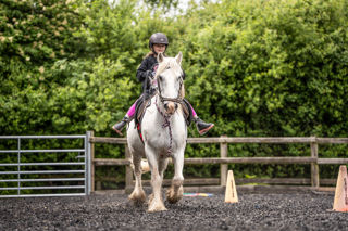 An image of a girl riding a small white horse around Cantref Riding Centre's training area.