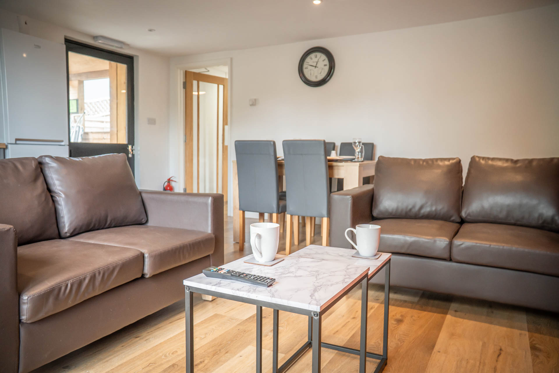 An image of a bright living area in a converted Hayloft, with wooden floors, two leather sofas, coffee table and dining table in the background.