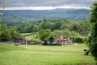 A landscape wide shot of the sand and water outdoor play area at Cantref Adventure Farm, with a lovely view behind.