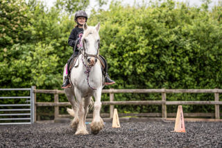 An image of a girl riding a small white horse around Cantref Riding Centre's training area.