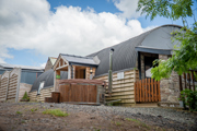 An image of a hayloft with a tin Barrell Vault roof and exterior wooden cladding. Converted into accommodation with an entrance porch, outdoor wooden fired hot tub and a small lawned area for outdoor games.