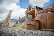 An image of a hayloft with a tin Barrell Vault roof and exterior wooden cladding. Converted into accommodation with an entrance porch, outdoor wooden fired hot tub and a small lawned area for outdoor games.