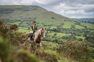 An image of the ride guide on horseback against a green backdrop of hills and bracken.