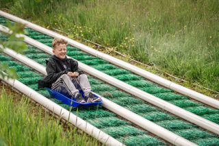 An image of a young boy zooming down the artificial grass, super sledge ride at Cantref Adventure Farm.