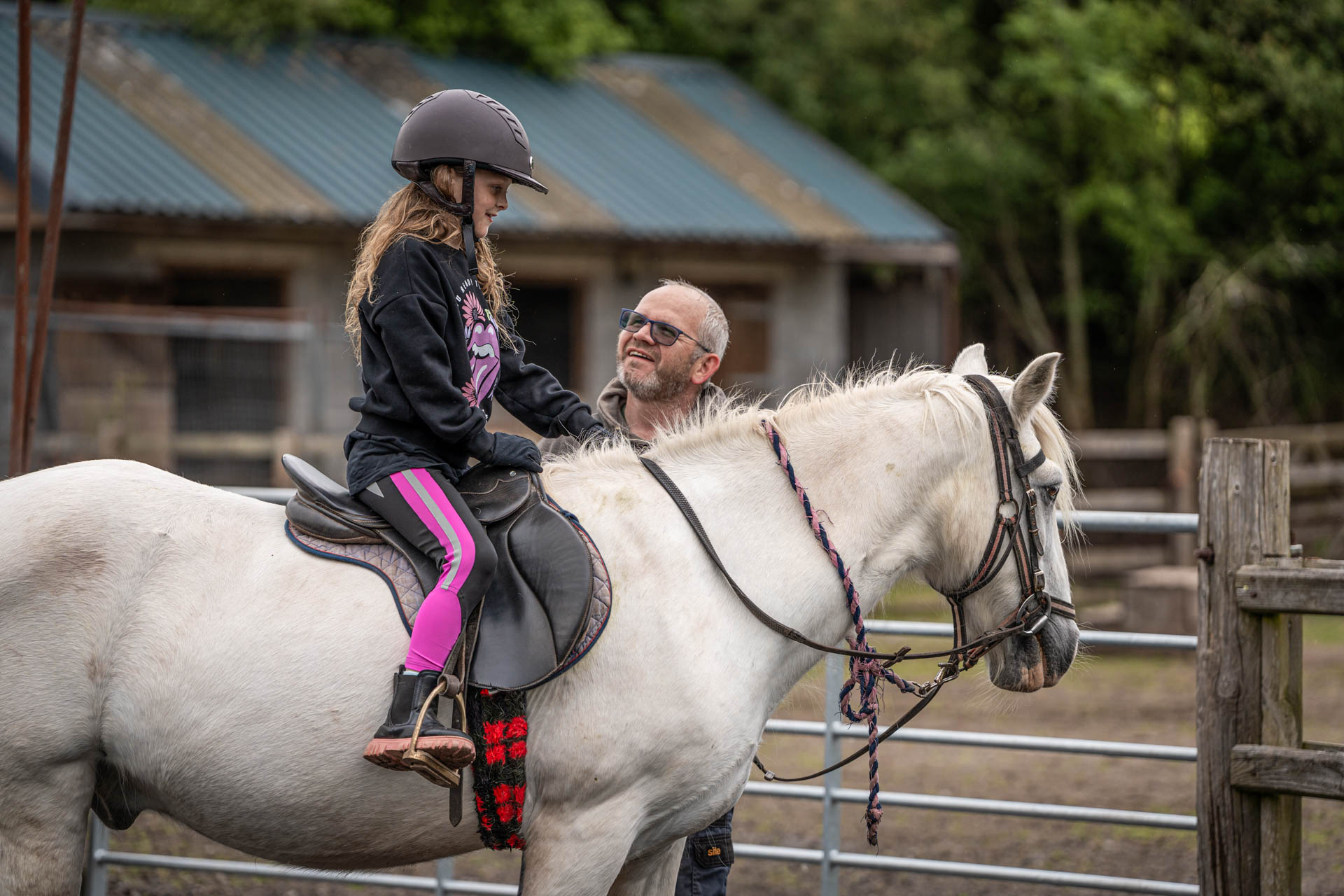 An image of a girl seated on a small white horse, having the reins checked by a member of the Cantref team.