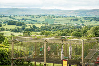 An image of the outdoor adventure bounce play area, with children bouncing up and down with a beautiful countryside backdrop.