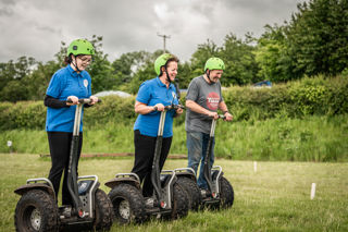 An image of a group of three using Segways on the grass practice field.