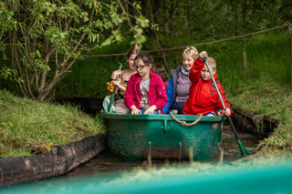 An image of four children and an adult in a green row boat, going round a jungle swamp course at Cantref Adventure Farm.