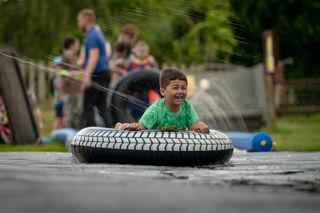 An image of a boy on an inflatable doughnut, sliding down a soapy slide, with a massive smile on his face.