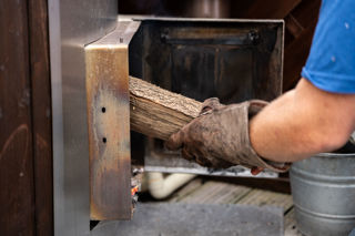An image of a Cantref team member putting another log into a wood-fired hot tub.