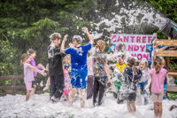 An image of the foam canon shooting out white foam which is covering the children standing underneath it and creating a blanket of sudds on the floor.