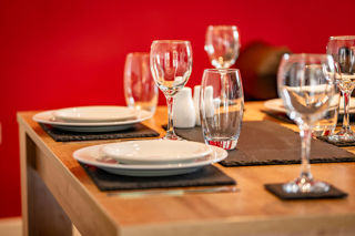 A close up image of a dining table set for four with a feature red wall behind.