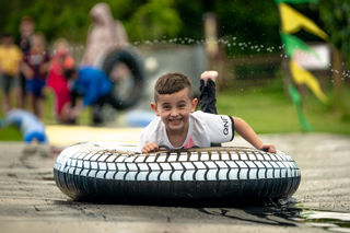 An image of a boy on an inflatable doughnut, sliding down a soapy slide, with a massive smile on his face.