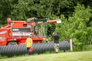 An image of a child sitting in the cab of a red combine harvester, pretending to drive it, whilst family take photos from outside.