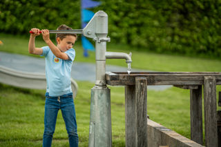 An image of a boy using a hand water pump to move water down a series of wooden channels.