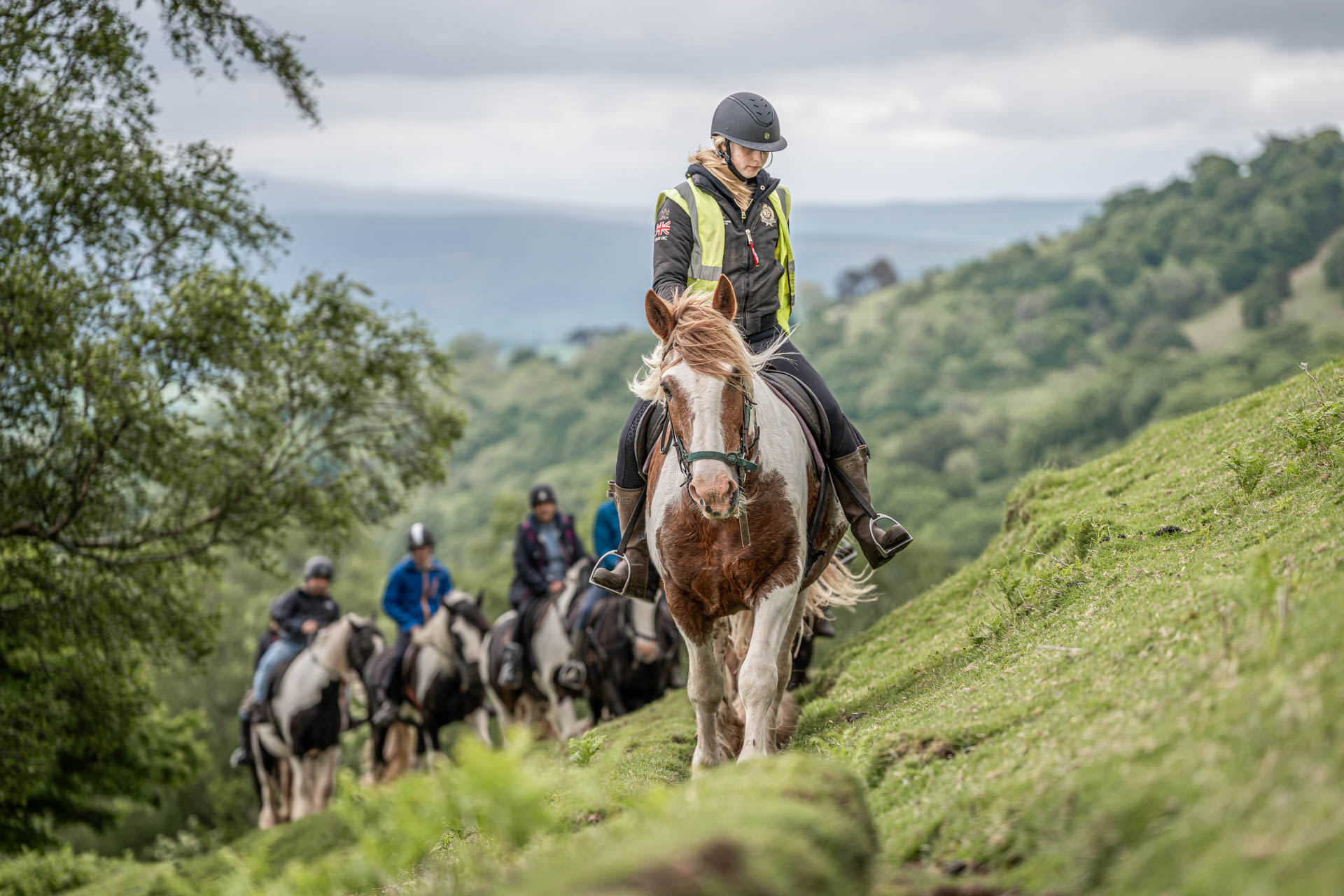 An image of guide leading a line of riders on horseback, single file, up and over the Brecon Beacons.