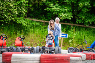 An image of a boy being assisted by mum and gran to ride a pedal go kart at Cantref Adventure Farm.