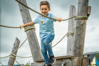 A close up image of a boy enthusiastically heading onto a rope bridge.